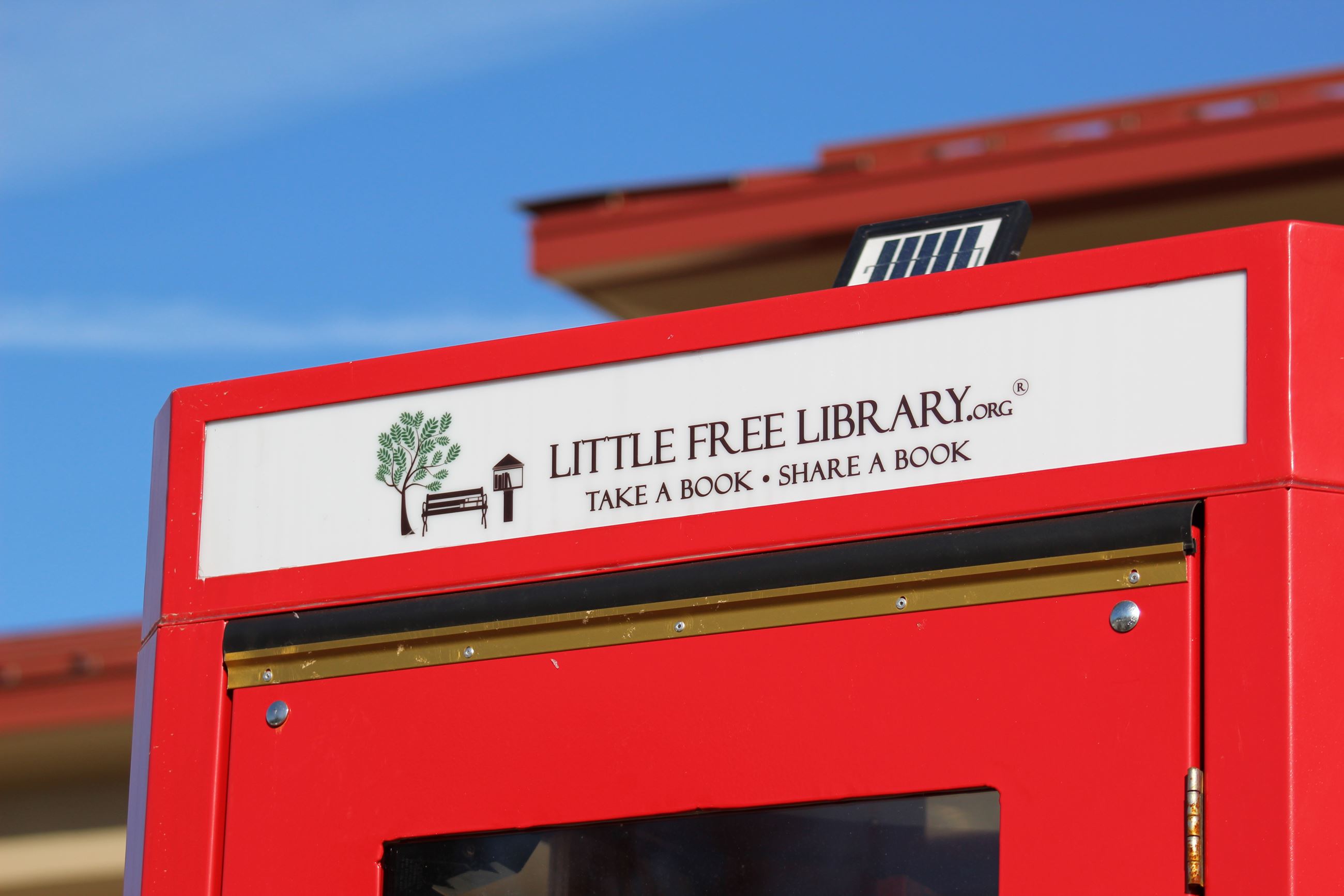 Top corner of a red phone booth with a sign advertising a LITTLE FREE LIBRARY