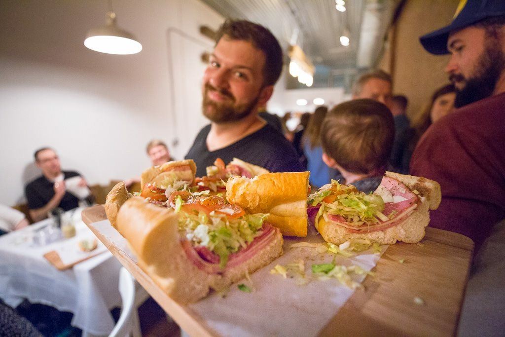 A restaurant owner reaches across the counter to offer a sandwich